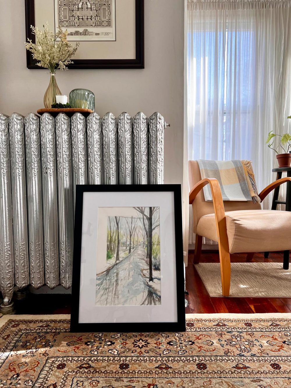 Watercolor landscape painting titled After the Storm by Samantha Eio in a black frame leaning against a silver radiator inside a cozy room
